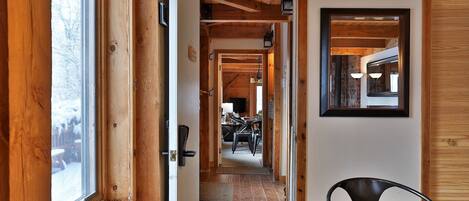 A wooden interior with a dining area, a mirror, and a view of a snowy landscape through a window.
