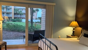 A hotel room with a bed, a chair, a lamp, and a view of the outdoor area.