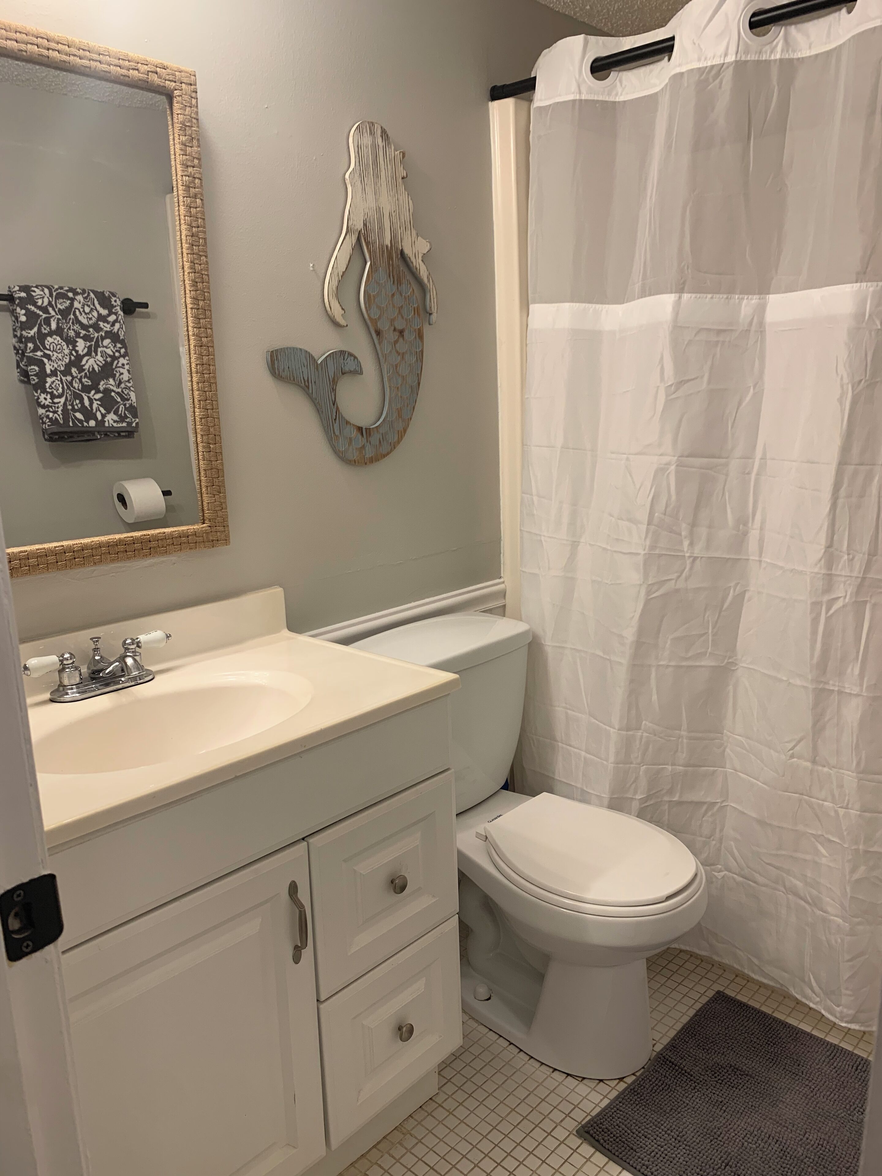 A bathroom with a white sink, a toilet, a decorative wall piece, and a shower curtain.