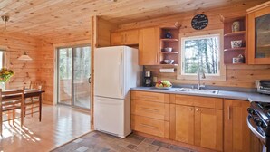 Cocina de cabaña de madera con refrigerador, pileta, alacenas y un comedor con mesa y sillas.