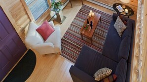 Interior acogedor de una cabaña con techo de madera, un sofá, un sillón, una mesita y un televisor.