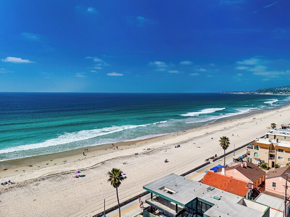 A beach with a clear view of the ocean, a sandy shore, and buildings in the foreground.