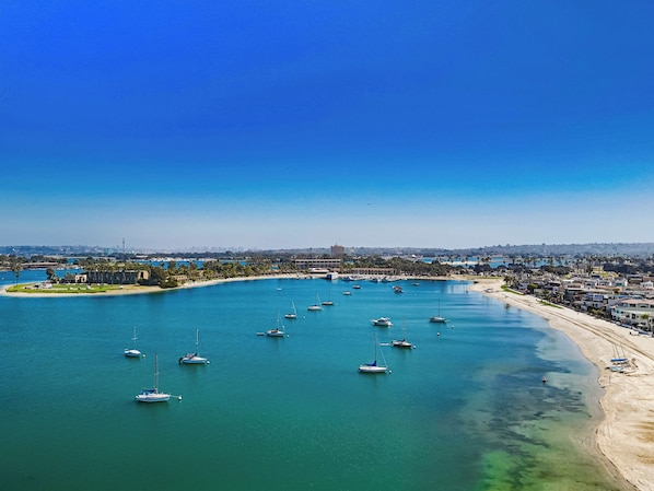 Un puerto deportivo con varias embarcaciones amarradas, una playa de arena y un paisaje urbano al fondo.
