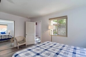 Un dormitorio con cama, una silla, una puerta que da a una escalera y una ventana con lámpara.
