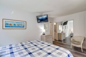 A bedroom with a bed, a television mounted on the wall, a dresser, a chair, and a mirror reflecting the room.