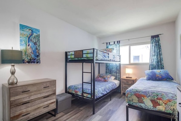 Una habitación con literas, un aparador de madera, una lámpara y un cuadro en la pared.