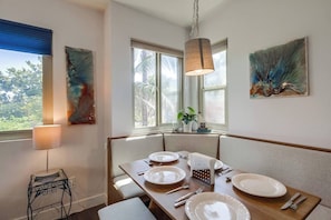 Un comedor con una mesa lista para cuatro personas, una ventana con vista a follaje y arte abstracto en la pared.