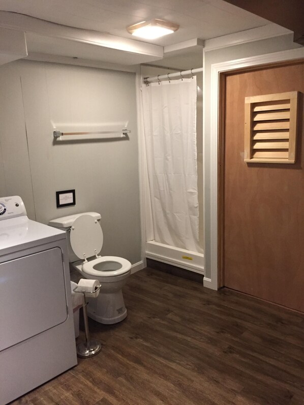 A bathroom with a toilet, a shower curtain, a wooden door, and a washing machine.