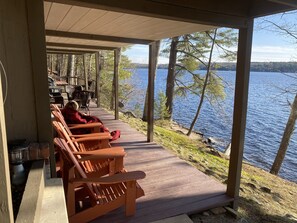 A wooden deck with chairs overlooking a lake, surrounded by trees.