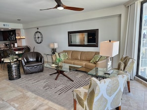 A modern living room with a glass coffee table, leather sofa, and a dining area with a kitchen in the background.