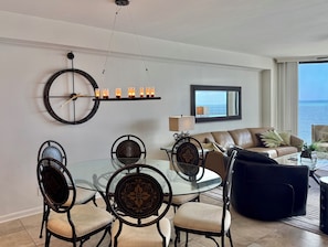 A modern living room with a dining area, a large round clock, and a view of the ocean.