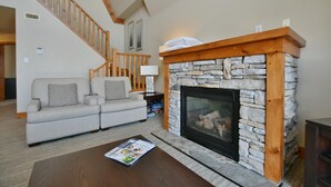 Ein Wohnzimmer mit Kamin aus Stein, einer Holztreppe und einem grauen Sofa.