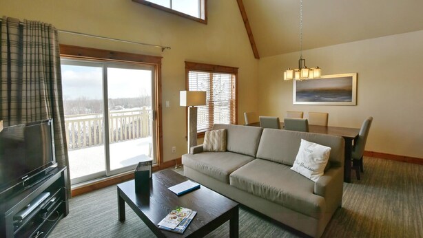 Ein Wohnzimmer mit einer Couch, einem Couchtisch, einem Fernseher und einem Balkon mit Aussicht.