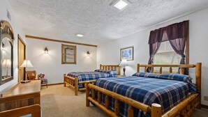 A room with two wooden beds, a wooden desk, a chair, a lamp, and a window with curtains.