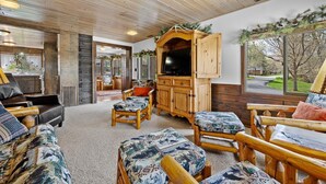 A cozy living room with a large TV, wooden furniture, and a view of the outdoors.
