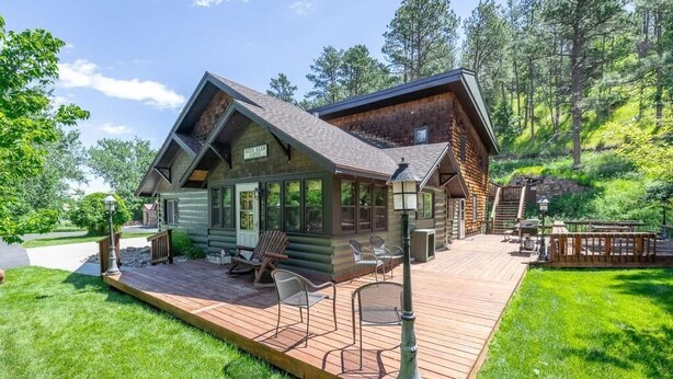 A log cabin with a deck, outdoor seating, and a scenic forest backdrop.