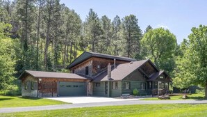 A two-story log cabin with a green exterior, a garage, and a front porch.