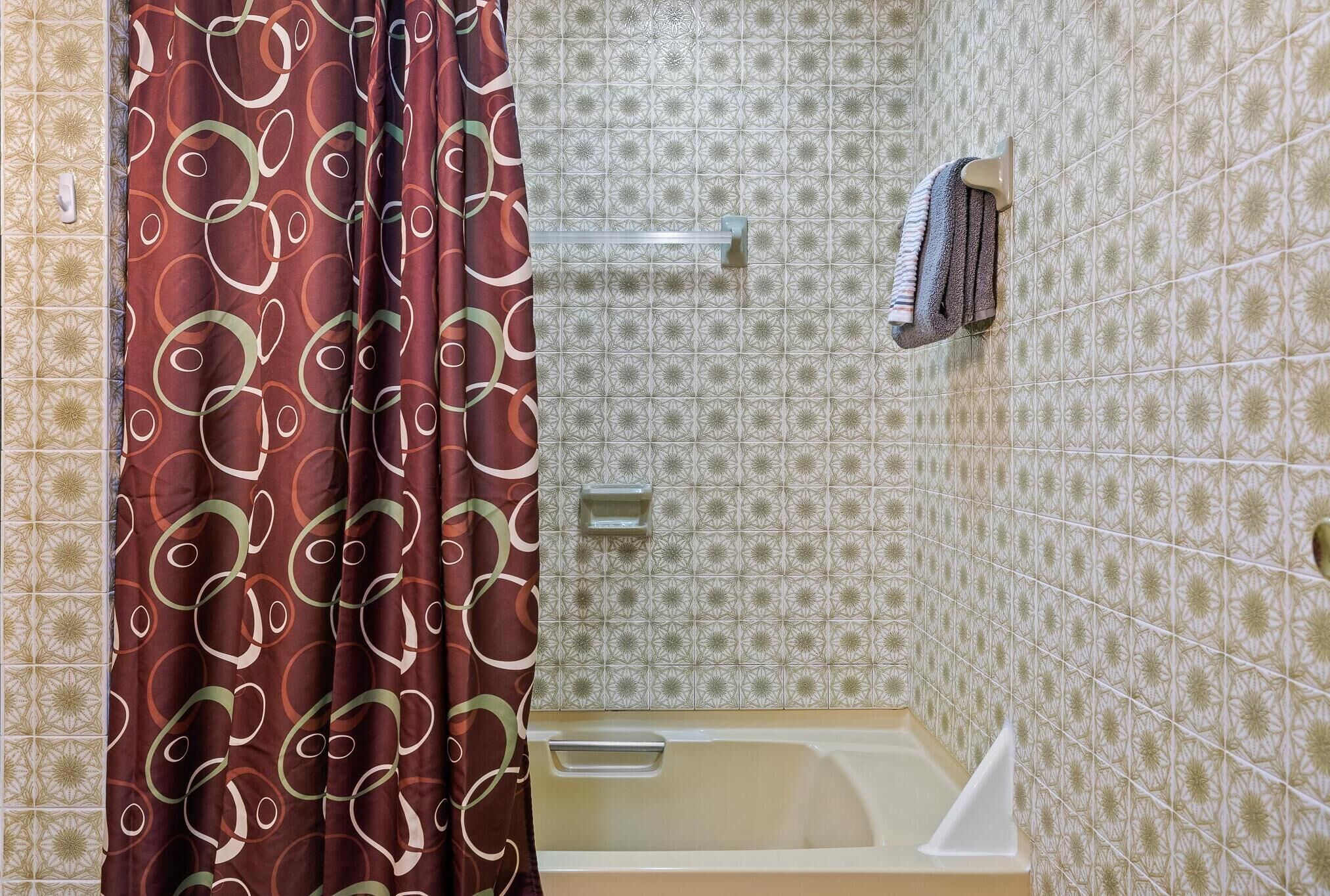 Un baño con baldosas estampadas, una bañera, una cortina de ducha y toallas colgadas en un perchero.