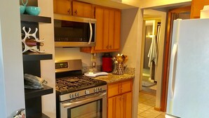 Une cuisine compacte équipée d’une cuisinière, d’un four à micro-ondes et d’un four traditionnel. On y trouve des armoires en bois et un sol carrelé.