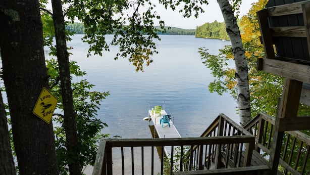 Une terrasse en bois offrant une vue sur un lac, un panneau jaune et une jetée avec des chaises.