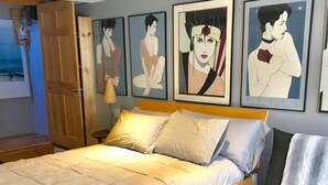 Une chambre à coucher avec un lit en bois, plusieurs oreillers, une table de chevet et des œuvres d’art murales.