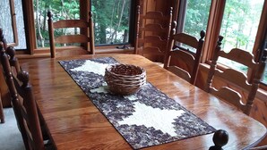 Uma mesa de jantar de madeira com um centro de mesa tecido, rodeada por cadeiras de madeira com assentos acolchoados.