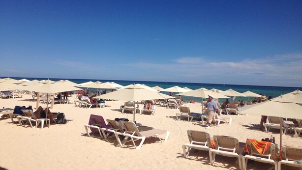 A beach with rows of sun loungers and umbrellas, a clear blue sky, and the ocean in the background. - Charming Mexican Style Condo with a fantastic location (Playa del Carmen)
