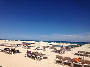 Une plage bordée de rangées de chaises longues et de parasols, un ciel bleu azur et l’océan en toile de fond.