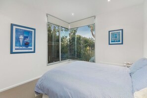 A bedroom with a large bed, a window with a view of trees, and two framed pictures on the wall.