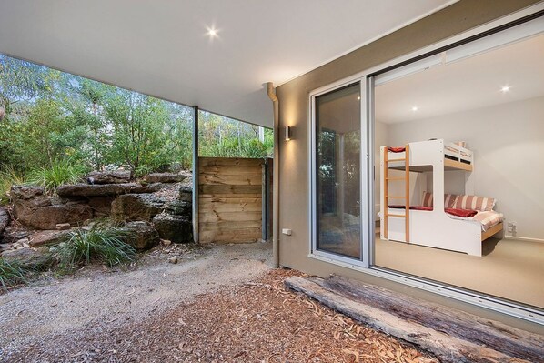 A modern house with a large glass door leading to a room with a bunk bed.