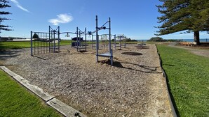 A playground with various equipment, a bench, and a view of the ocean. - Southern Escape - A Family Friendly Home 3 minute walk to  the Beach  (VICTOR HARBOR)