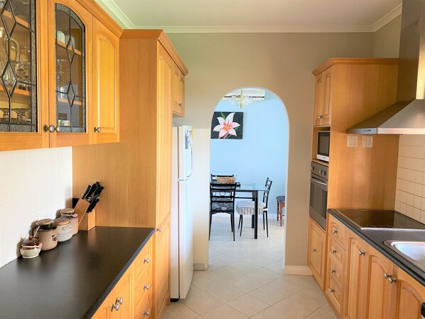 A kitchen with wooden cabinets, a refrigerator, a dining table with chairs, and a tiled floor.