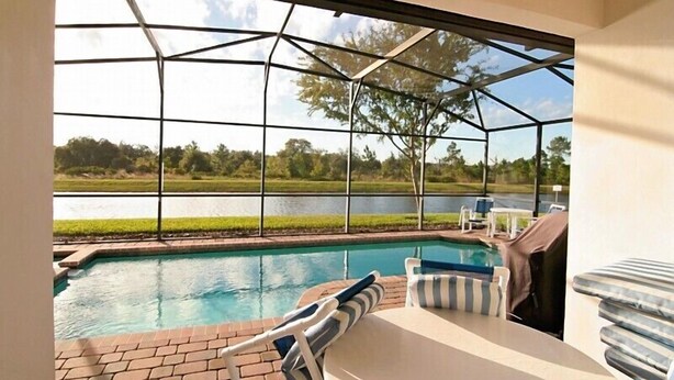 A covered outdoor area with a pool, lounge chairs, and a view of a lake. - A gorgeous lake sunset view villa in a gated High Grove resort near Disney (Clermont)