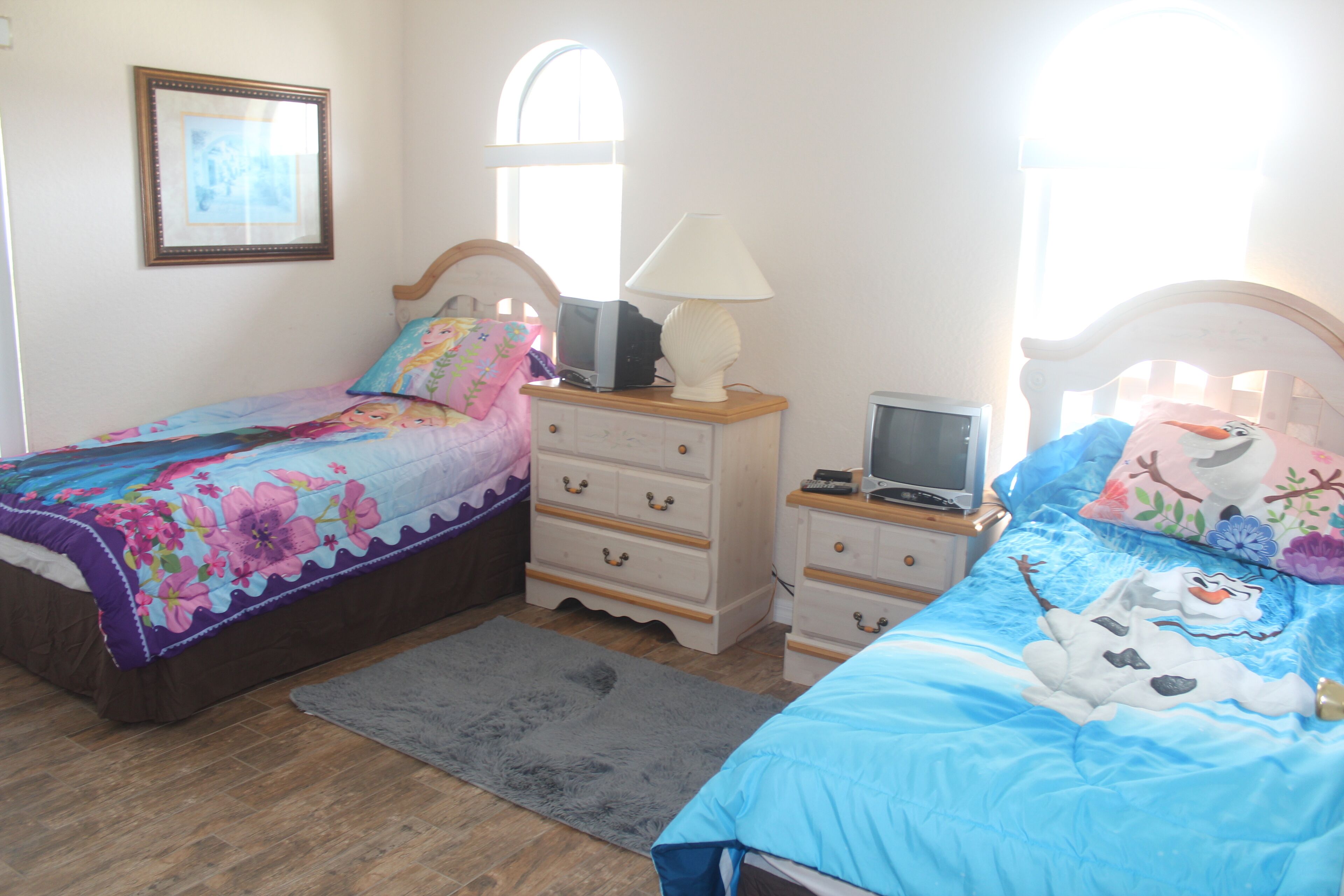 Une chambre avec deux lits, une commode, une lampe et un téléviseur.