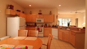 A compact kitchen with wooden cabinets, a microwave, a stove, and a dishwasher. There is a dining table with chairs and a window providing natural light. - A gorgeous lake sunset view villa in a gated High Grove resort near Disney (Clermont)