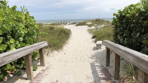 Un sentier de plage sablonneux, bordé de rambardes en bois de chaque côté, qui mène à l’océan.