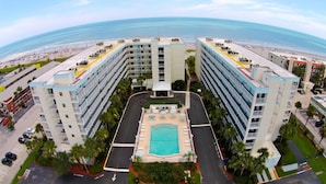 Un grand hôtel à plusieurs étages, doté d’une cour intérieure avec une piscine et offrant une vue sur la plage.