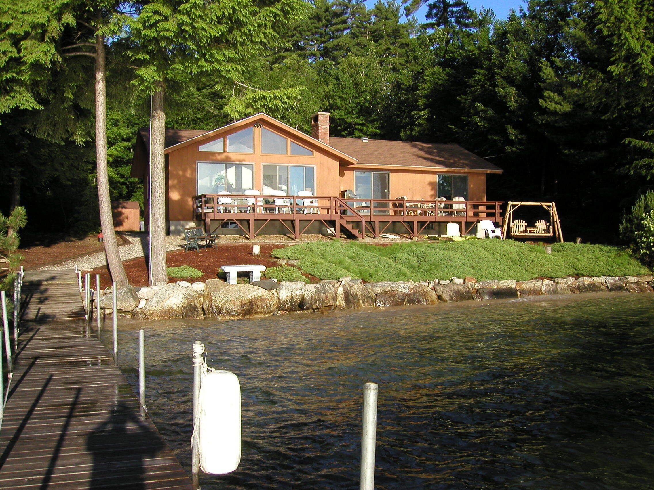 A lakeside cabin with a deck, a dock, and a swing set.