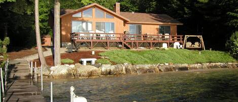 A lakeside cabin with a deck, a dock, and a swing set.