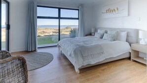 A bedroom with a large bed, a ceiling fan, a view of the outdoors, and a wall-mounted artwork. - ABSOLUTE BEACHFRONT - Smooth Sailing Yorke Peninsula (Coobowie)