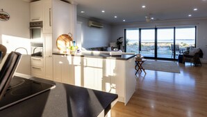 A modern kitchen with a central island, built-in appliances, and a large sliding glass door leading to a balcony with a view of the beach. - ABSOLUTE BEACHFRONT - Smooth Sailing Yorke Peninsula (Coobowie)