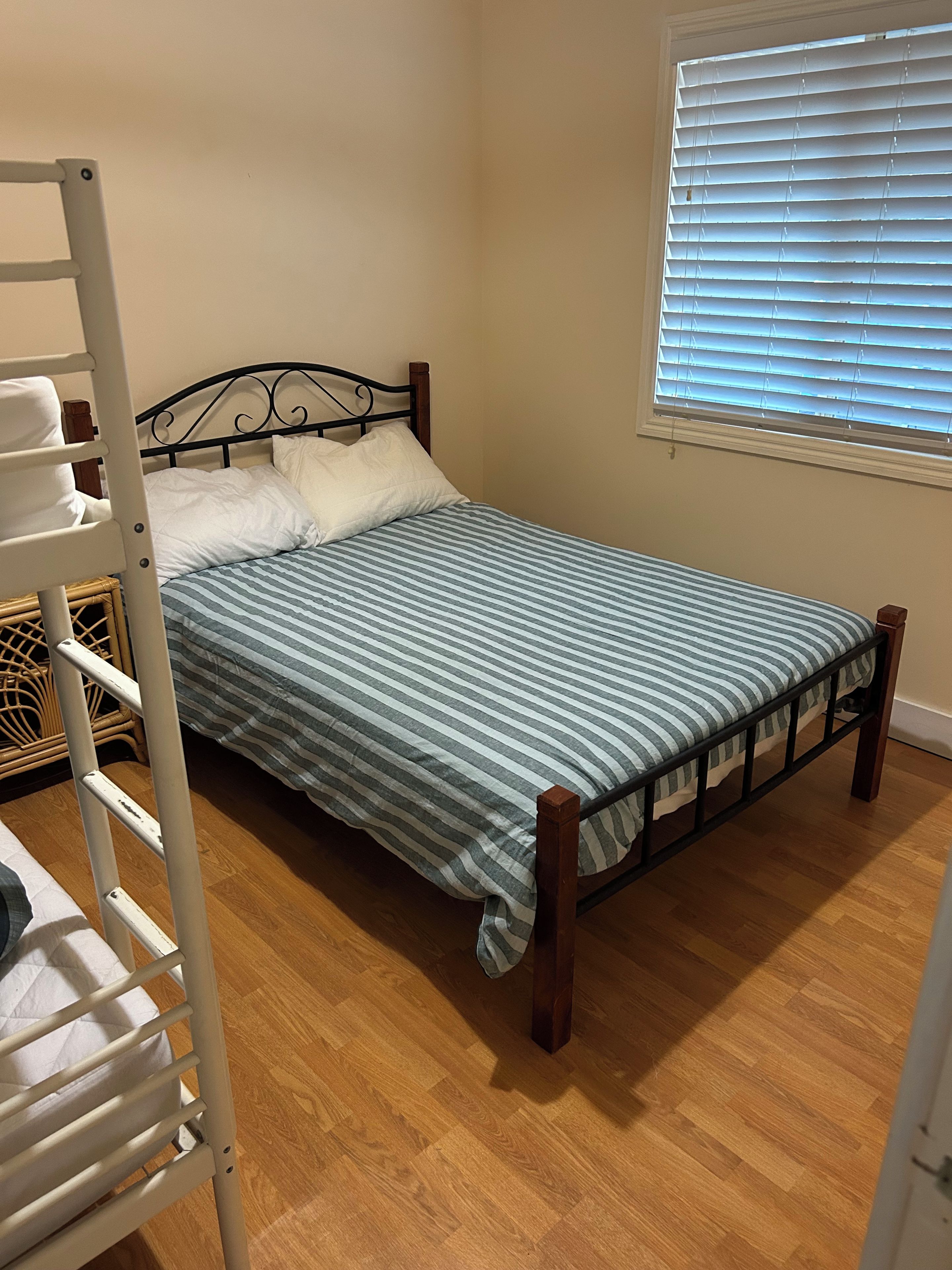 A single bed with a striped bedspread, a wooden headboard, and a window with blinds.