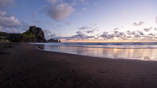 Una playa con un promontorio rocoso y agua tranquila que refleja el cielo.