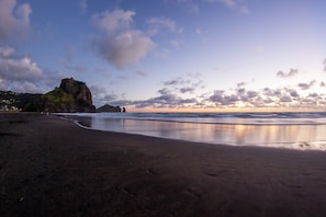 A beach with a rocky outcrop and calm water reflecting the sky.