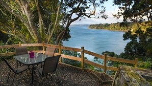 Un área de estar al aire libre con una mesa y sillas, con vista a una masa de agua rodeada de árboles.