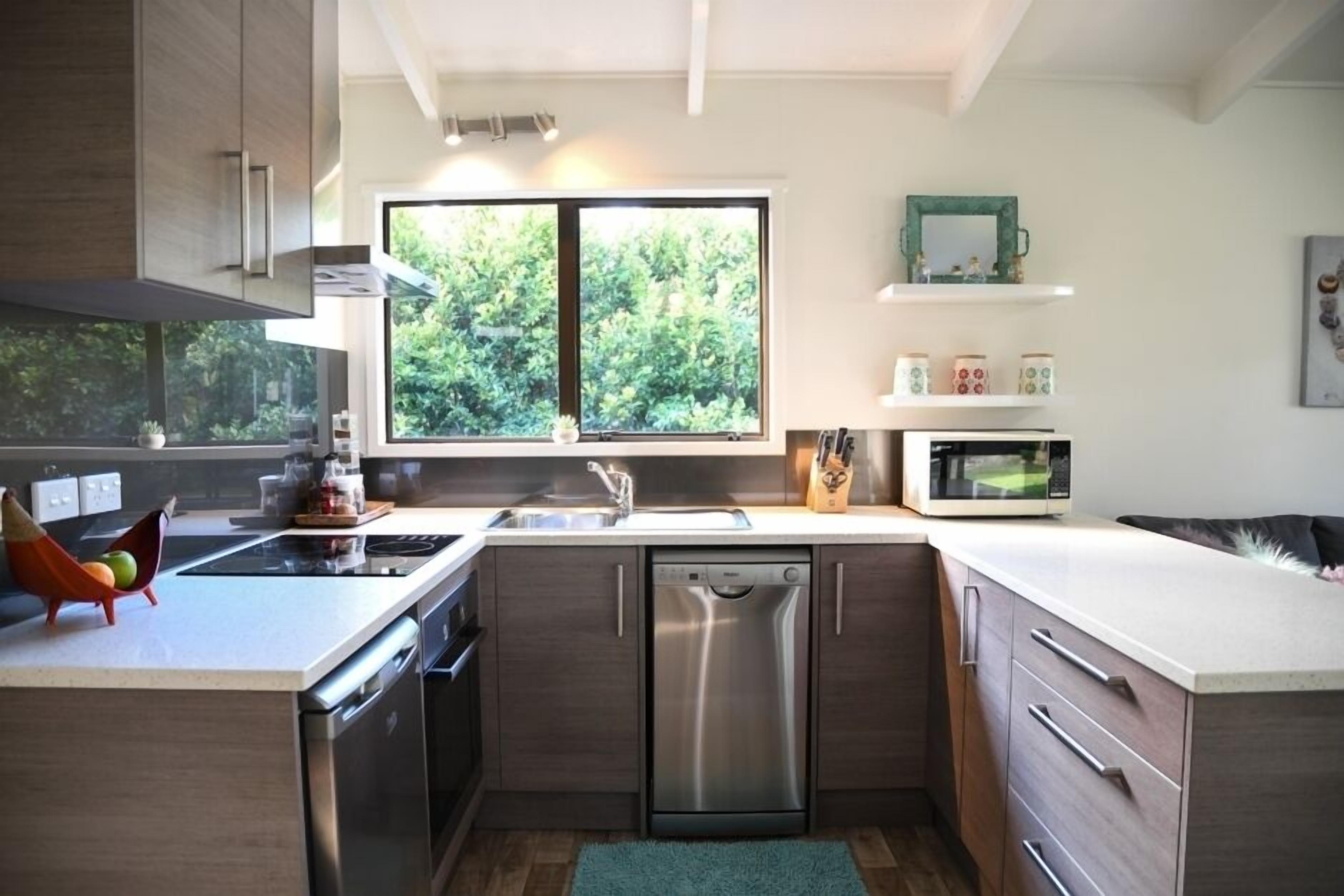Una cocina moderna con lavavajillas, microondas y ventana con vistas a zonas verdes.