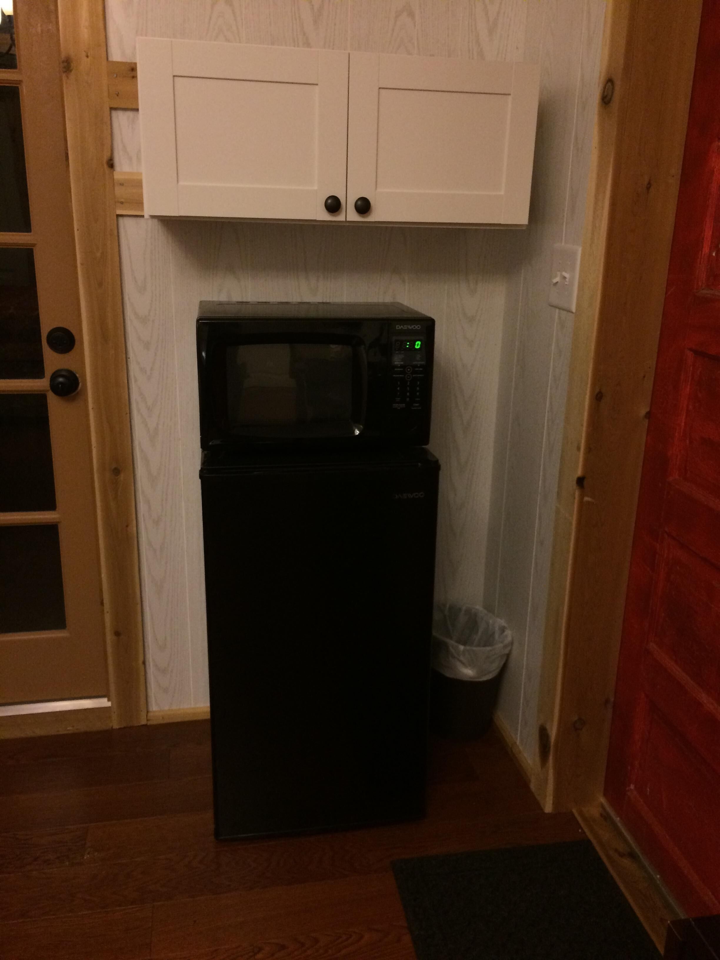 A compact kitchen with a black refrigerator and microwave, a white cabinet above, and a wooden door with a glass panel.