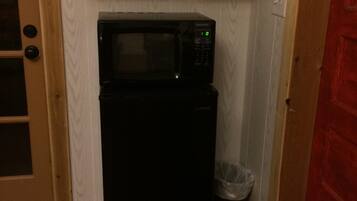 A compact kitchen with a black refrigerator and microwave, a white cabinet above, and a wooden door with a glass panel.
