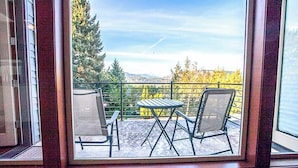Un balcon avec deux chaises et une table, offrant une vue panoramique sur les arbres et les montagnes.
