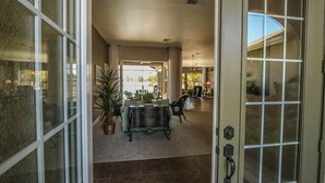 Puerta abierta que da a un comedor con una mesa, sillas, una planta en maceta y vistas al exterior.